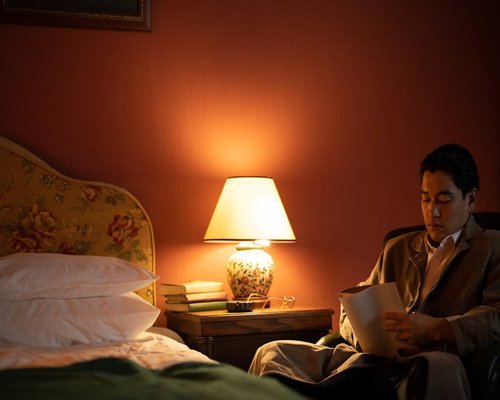 A person reading a book in bed with a warm bedside lamp illuminating the room
