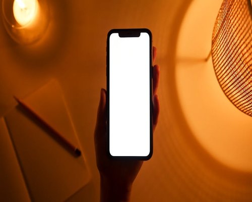 A person holding a smartphone on a dark background with warm display light